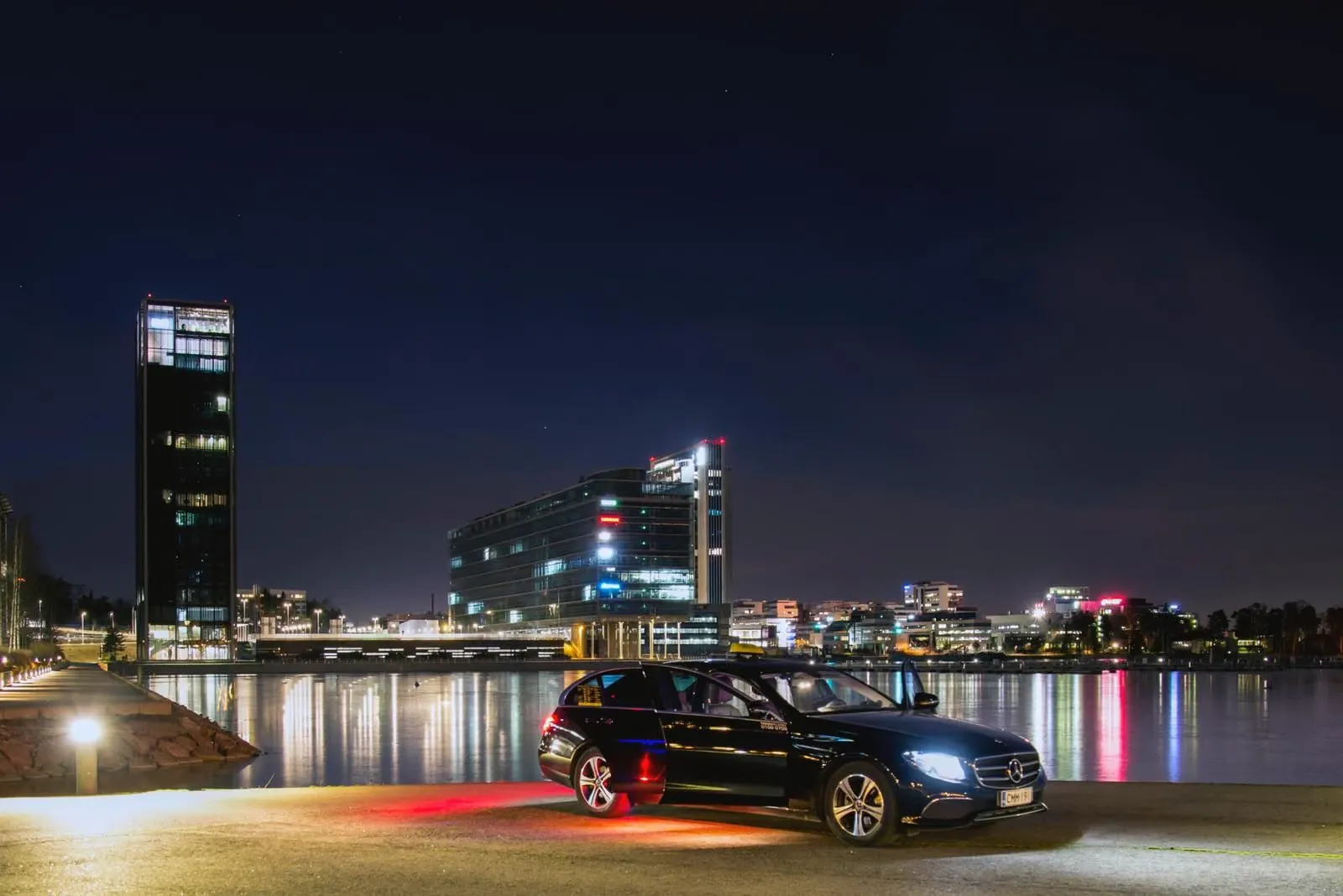 Mercedes-Benz E-sarja illalla rannassa kaupungin valojen edessä